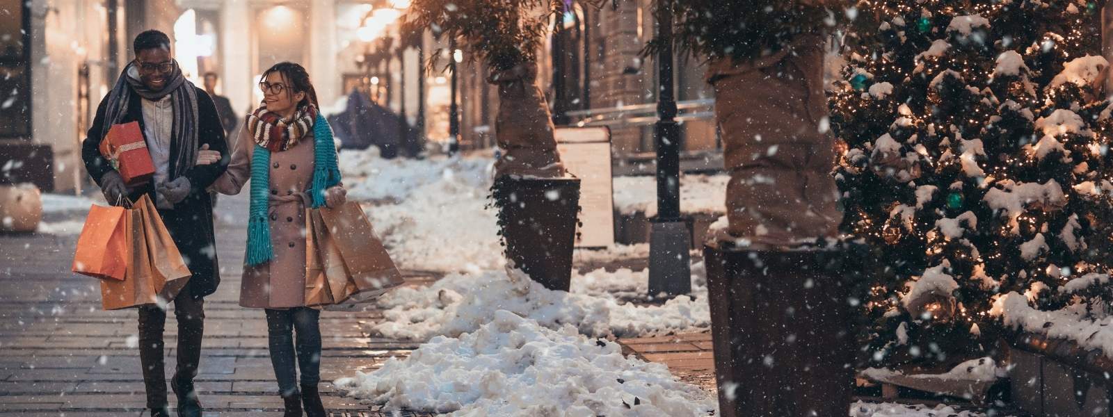 couple walking down a snowy sidewalk carrying gift